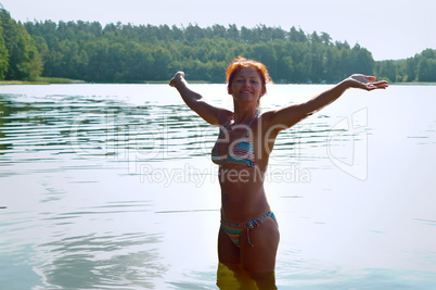 girl with outstretched hands in the swimsuit at the lake, a girl smiling at lake in summer