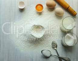 Eggs, flour, milk, sugar, on a white wooden table.