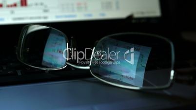 Business background. Glasses with reflection of stock trading data on a laptop keyboard.