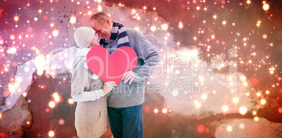 Composite image of happy mature couple in winter clothes holding red heart