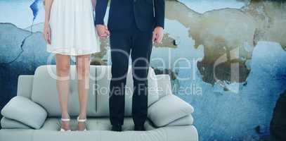 Composite image of low section of couple standing on sofa