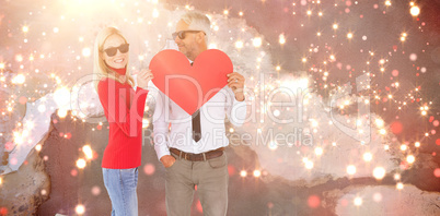 Composite image of cool couple holding a red heart together