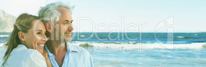 Happy couple hugging on the beach looking out to sea