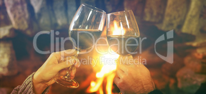 Cropped image of hands toasting wineglasses against fireplace