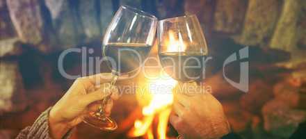 Cropped image of hands toasting wineglasses against fireplace