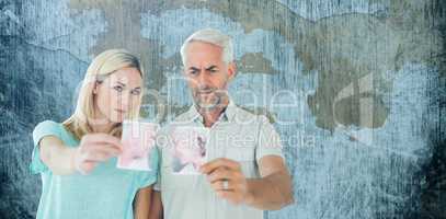 Composite image of unhappy couple holding two halves of torn photograph