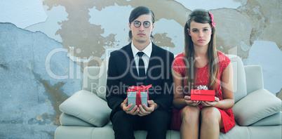 Composite image of unsmiling geeky couple with gift