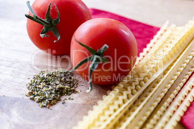 Dry spaghetti, fresh tomatoes and Italian herbs, closeup, high angle.