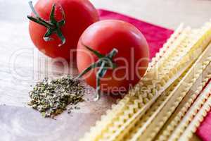 Dry spaghetti, fresh tomatoes and Italian herbs, closeup, high angle.