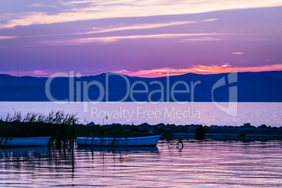 Vivid pink sunrise over calm lake and silhouette of rowing boats.