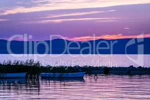 Vivid pink sunrise over calm lake and silhouette of rowing boats.