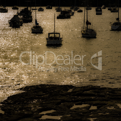 Golden sunset, reflections on water in calm bay, silhouette of sailing boats.
