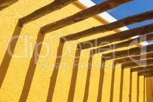 Abstract Wood Post Beams and Bright Yellow Wall Against Blue Sky