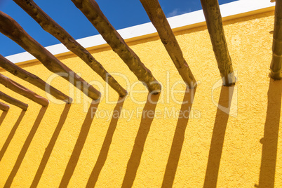 Abstract Wood Post Beams and Bright Yellow Wall Against Blue Sky