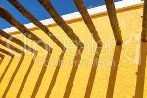 Abstract Wood Post Beams and Bright Yellow Wall Against Blue Sky