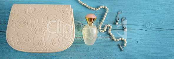 A handbag and a bottle of perfume on a blue wooden background. W
