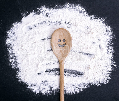 spoon with a carved smiling face lies on scattered flour