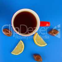 Red cup with tea , lemon slices and chocolate candies on a blue