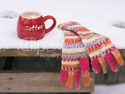 multi-colored knitted mittens and a red cup with coffee
