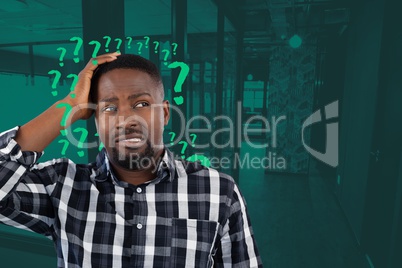 Confused man holding his head looking on the right in an office with question marks