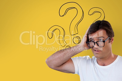 Confused man with glasses holding his head on yellow background with question marks