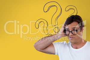 Confused man with glasses holding his head on yellow background with question marks