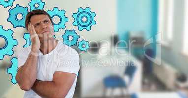 Confused man frowning and holding his head looking up in an office with cogs