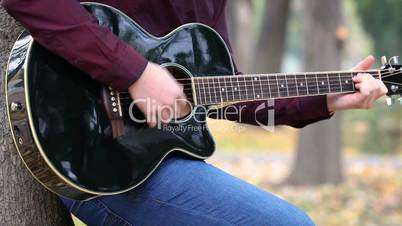 Young man playing acoustic guitar artist musician outdoors