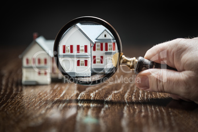 Hand Holding Magnifying Glass Up To Model Home on Reflective Woo