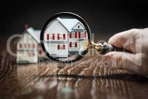 Hand Holding Magnifying Glass Up To Model Home on Reflective Woo