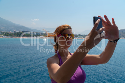 Attractive young girl taking a selfie portrait with cell phone on the boat, smiling.