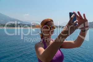 Attractive young girl taking a selfie portrait with cell phone on the boat, smiling.