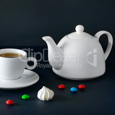 White cup and tea pot on a black background.
