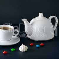 White cup and tea pot on a black background.