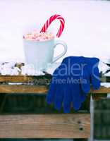 cup with hot chocolate and marshmallow on a snow-covered table