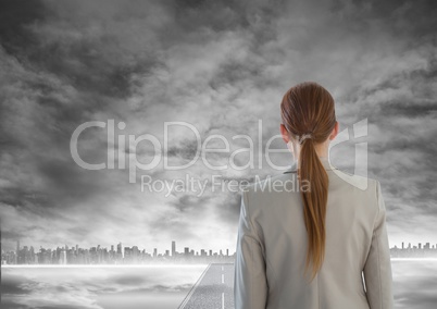 Woman looking out at grey city skyline with road leading to city underneath smoke