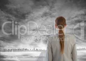 Woman looking out at grey city skyline with road leading to city underneath smoke