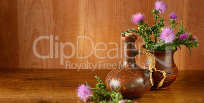 Oil and flowers of milk thistle on wooden background.