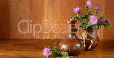 Oil and flowers of milk thistle on wooden background.