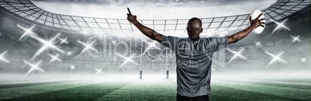 Composite image of rear view of sportsman with arms raised holding rugby ball