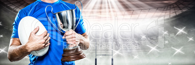 Composite image of rugby player holding trophy and ball