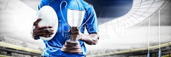 Composite image of mid section of sportsman holding trophy and rugby ball
