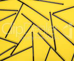 black cocktail straws scattered on a yellow background
