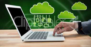 Hand using laptop with clouds icon and hanging connection devices and green background