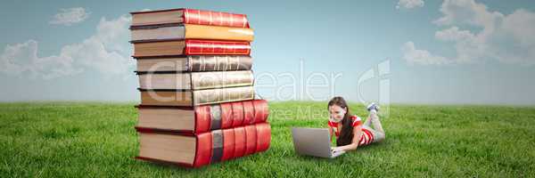 Woman using computer and laying on the floor next to a pile of books outdoors