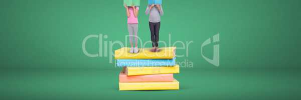 Two girls reading and standing on a pile of books with green background