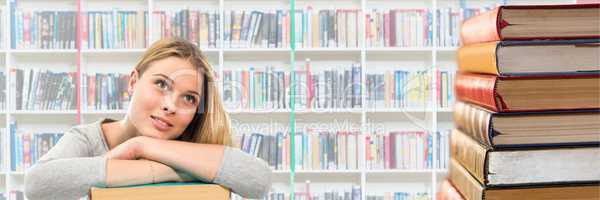 Young woman in a library looking up and a pile of books