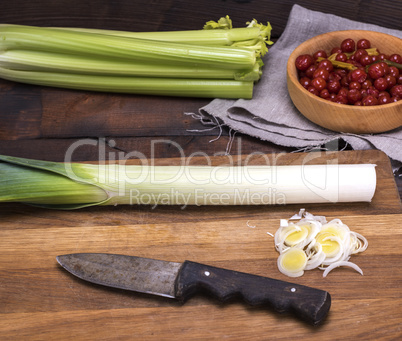 Sliced green onions on a wooden board, behind bunches of celery