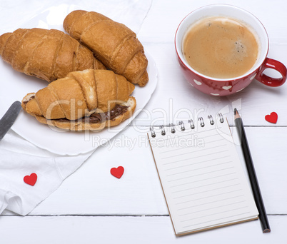 red ceramic mug with hot coffee and fresh croissants