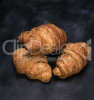 three baked croissants on a black background